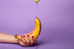 A hand pours personal lubricant over a banana